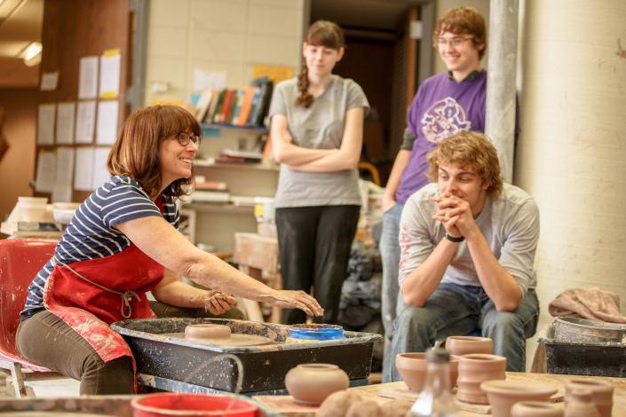 Prof. Kimberly Greene demonstrates to students how to throw clay in a pottery class.